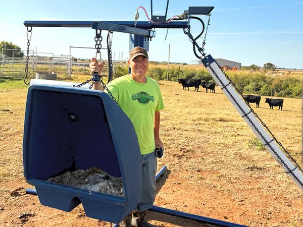 Rancher standing beside a Lewis cattle oiler with cattle in the background