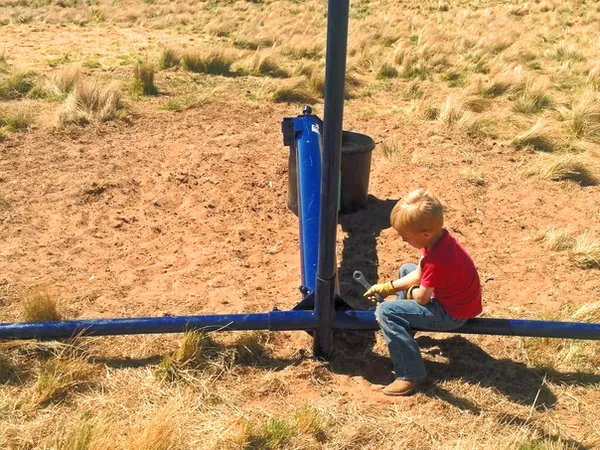 Young child sitting beside a Lewis cattle oiler in a dry pasture